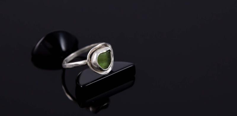 Photograph of a silver ring with a green stone on a black surface.