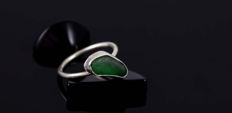 Photograph of a silver ring with a green sea glass stone on a black surface.