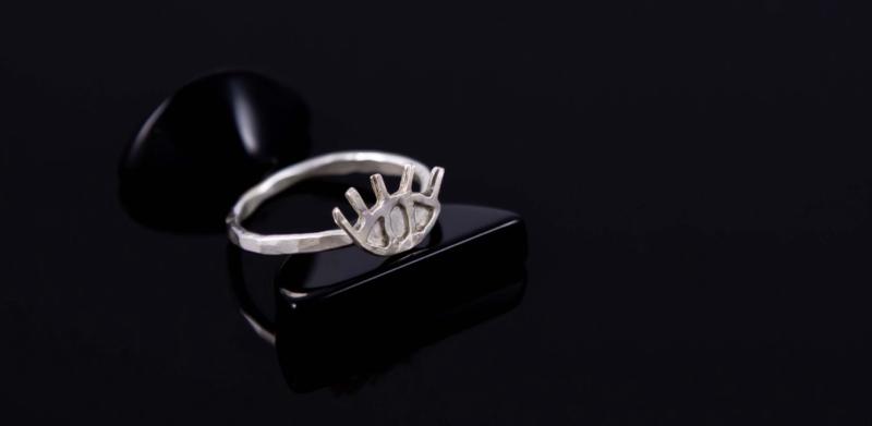 A silver ring with an eye design rests on a black stand.
