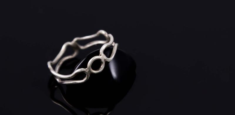 Photograph of a silver ring with interconnected loops on a black reflective surface.