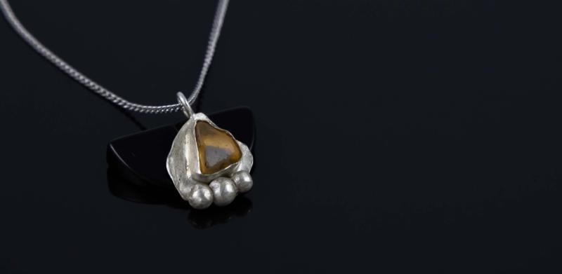 Photograph of a silver pendant with a gemstone on a black background.