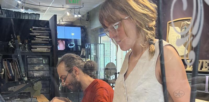 Photograph of two artisans working in a workshop with a torch, viewed through a patterned glass.