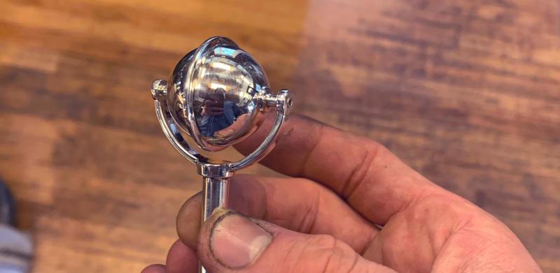 Photograph of a hand holding a small, shiny metal baby rattle.