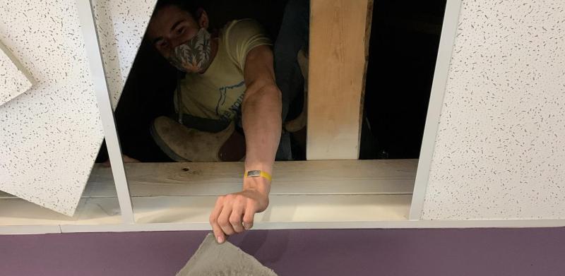 A person crouches in a ceiling opening, holding an air filter.