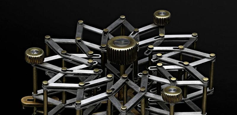 A complex, radial mechanical device of interlocking brass and silver bars against a black background.