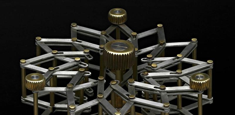 A complex, radial mechanical device of interlocking brass and silver bars against a black background.