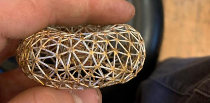 Close-up photograph of a hand holding a small, intricate, silver geometric donut..