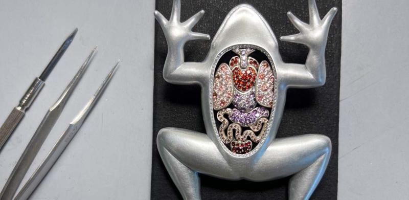 A silver frog figurine with an open chest exposing colorful jewels next to three metal tools.