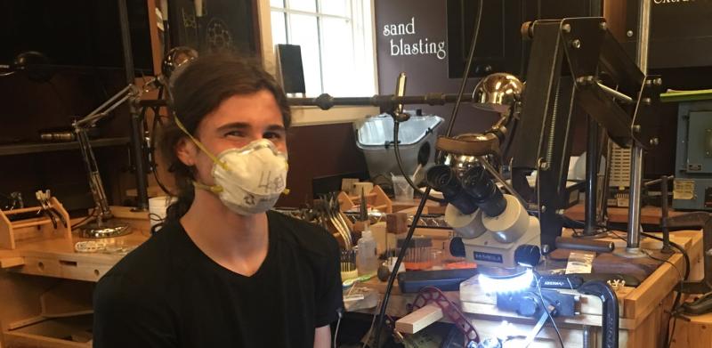 A young person wearing a mask sits in a well-equipped workshop.