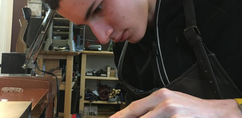 A young person filing metal at a workbench in a brightly lit workshop.