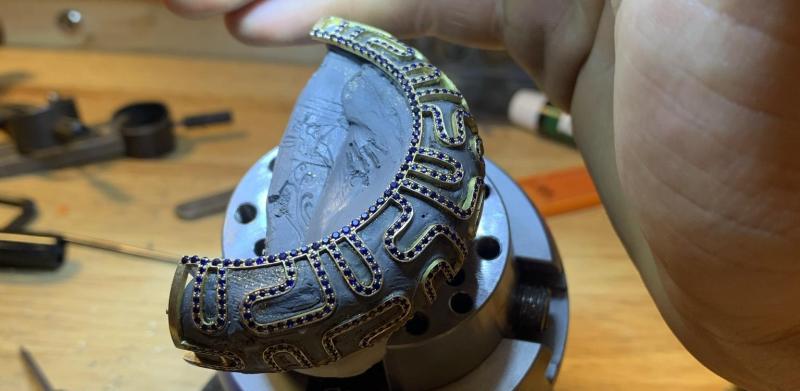 Photograph of a person shading an intricate bracelet on a jeweler's block.