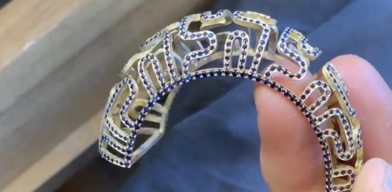 A hand holding an ornate gold bracelet encrusted with blue stones.