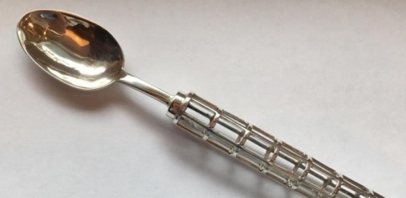 A silver spoon with an ornate, caged handle on a white surface.