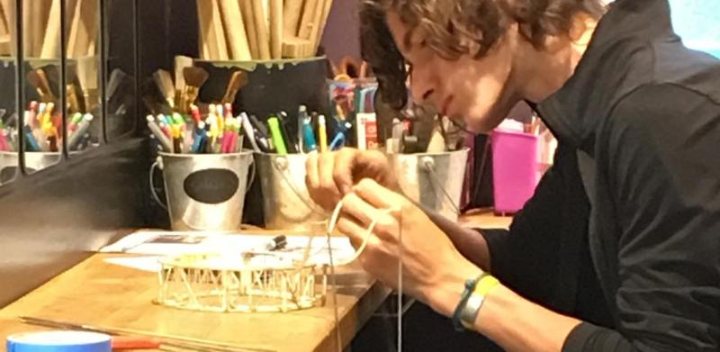 A person with curly brown hair works intently at a workbench in a bright studio.