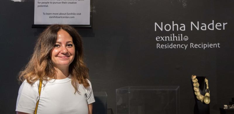 Photograph of a woman smiling in front of an art exhibition wall.