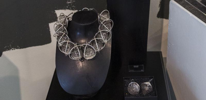 Photograph of silver jewelry displayed on black stands in a gallery.