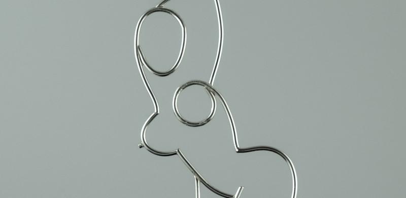 Photograph of a wire pendant shaped like a woman's body on a black cord.