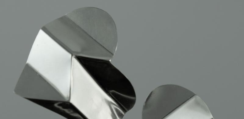 Two silver, geometric, heart-shaped earrings on a grey background.
