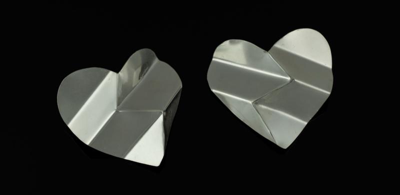 Two silver heart-shaped metal pieces with folded lines, set against a solid black background.