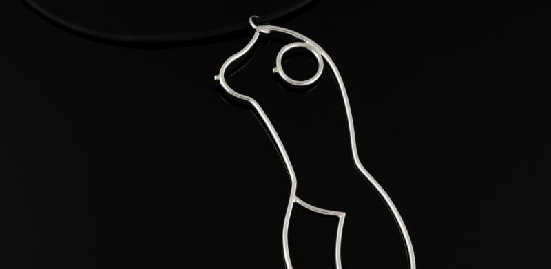 Photograph of a silver wire pendant shaped like a female body against a black background.