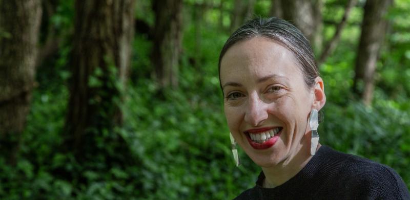 Photograph of a smiling woman in a lush green forest.