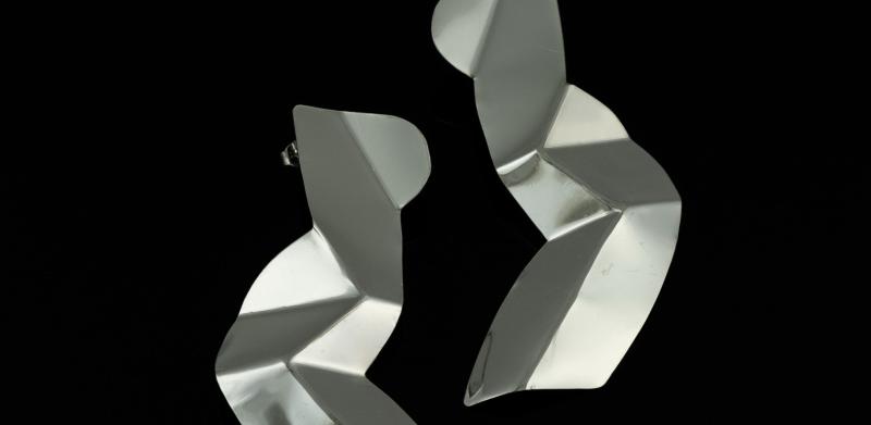 Photograph of two abstract silver earrings against a black background.