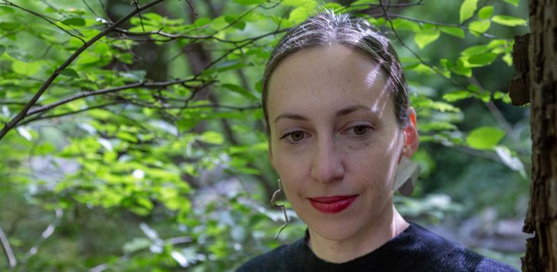 A photograph of a woman wearing a black sweater in a lush green forest.