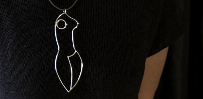A woman wearing a large, abstract female-form pendant necklace.