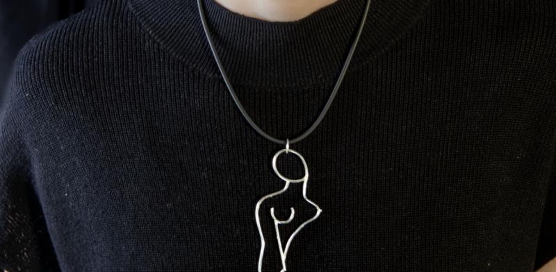 A woman in a black shirt wears a silver pendant resembling a human figure.