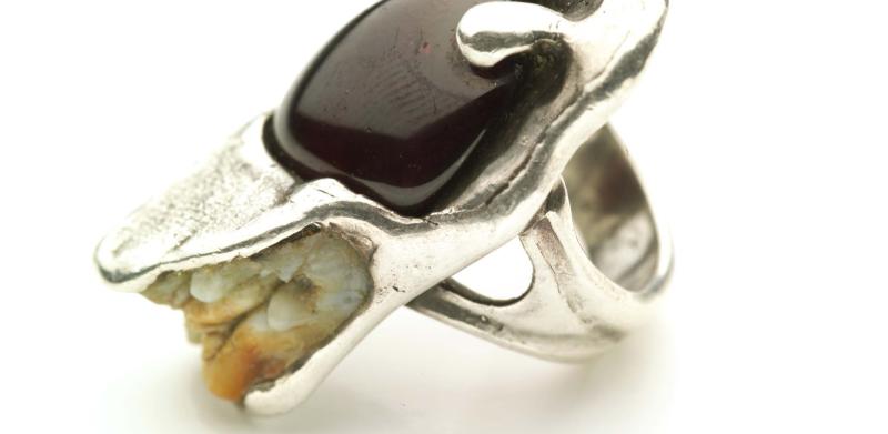 Photograph of a silver ring set with an garnet gemstone and a tooth.