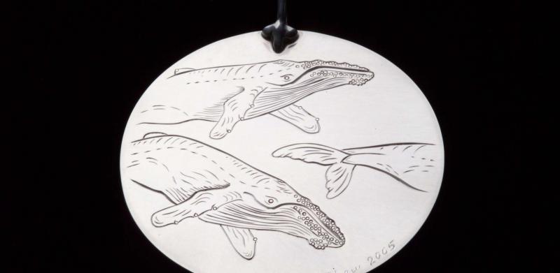 Circular silver pendant with etched illustration of three swimming whales.