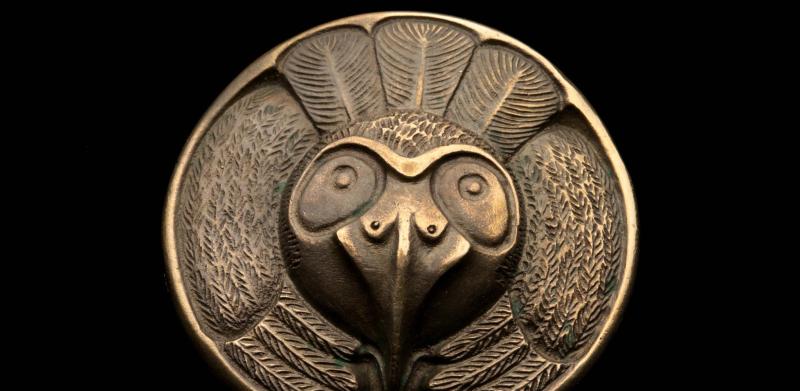 Photograph of a round bronze medallion featuring an owl face and feathers.