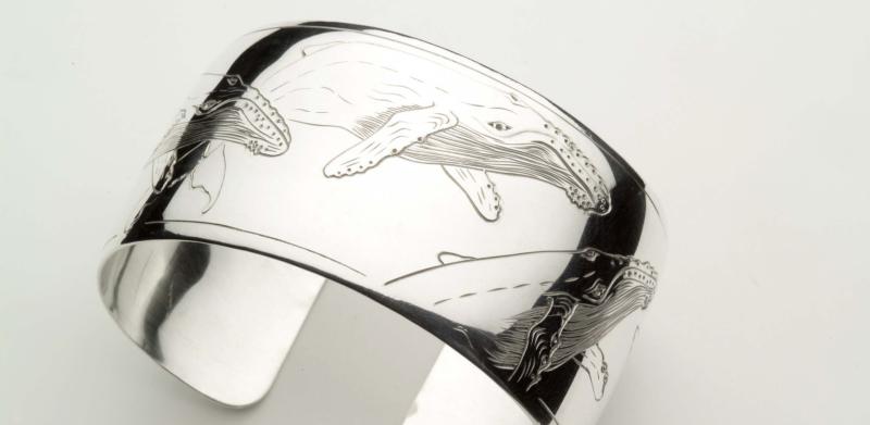 Photograph of a wide silver cuff bracelet engraved with a humpback whale design.