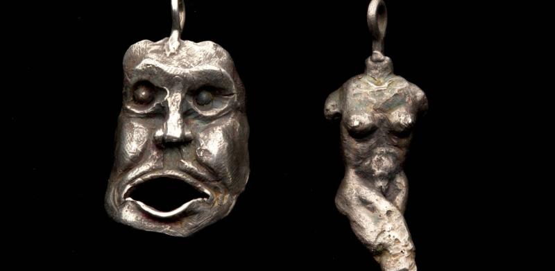 Photograph of two silver pendants: one shaped like a screaming face, the other like a torso.
