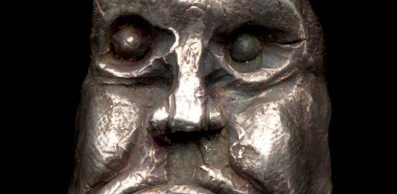 Photograph of a silver pendant shaped like an expressive, grotesque human face.
