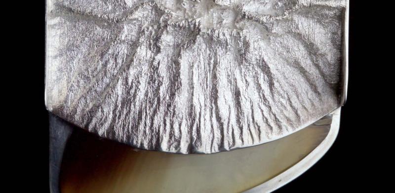 Photograph of a silver pendant with a textured rectangular top and a curved base made of moose hoof.