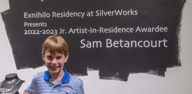 Photograph of a woman and boy smiling next to a pedestal with artwork.