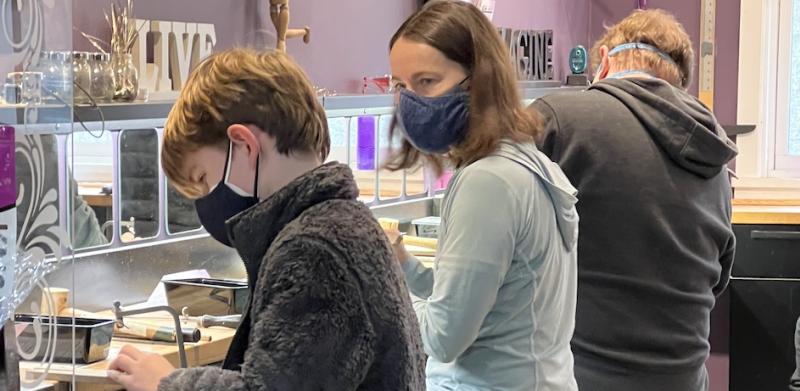 Photograph of three people wearing masks, working at stools in a bright, purple-walled workshop.