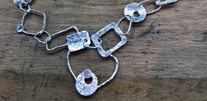 Photograph of a silver chain necklace with geometric shapes on a wooden surface.