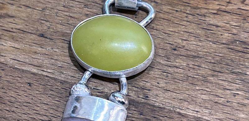 Photo of a silver pendant with a green and light pink stone on a wooden surface.