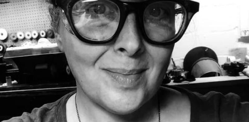 Black and white portrait of a smiling woman in thick glasses and a wave necklace.