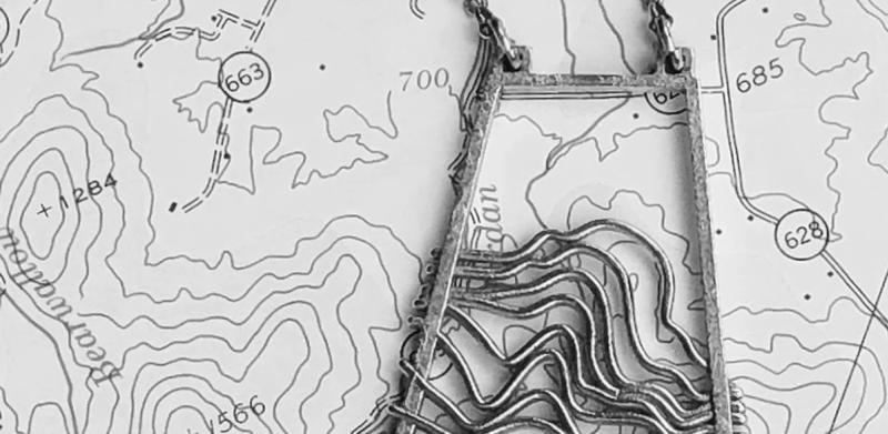 Black and white photo of a trapezoidal pendant necklace on a topographic map.