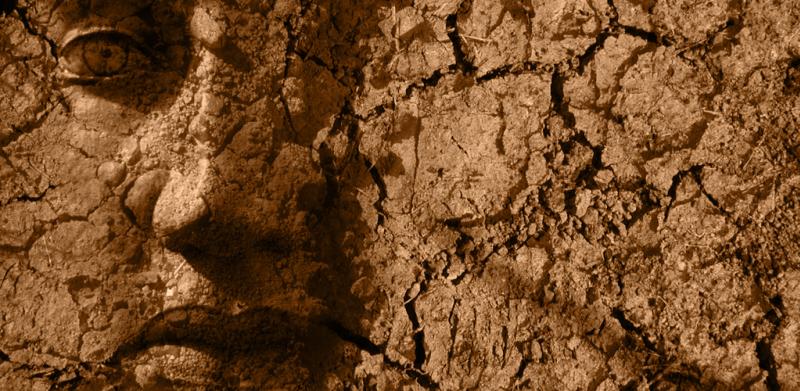 A human face merged with cracked, dry earth in sepia tones.
