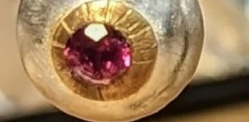 Photograph of a silver and gold earring featuring a round ruby gemstone.