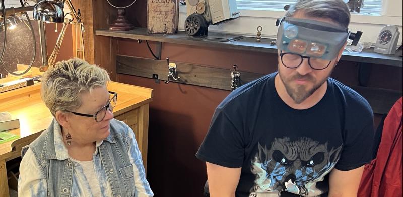 Photo of a man wearing magnifying headgear sitting next to a smiling woman in a workshop.