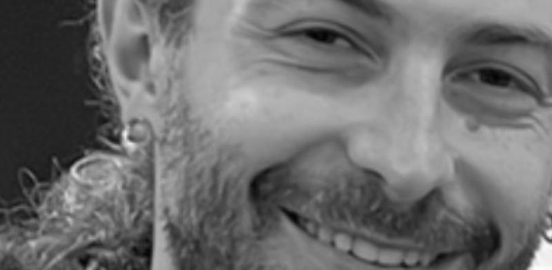 Black and white photograph of a smiling man with a beard and earring.