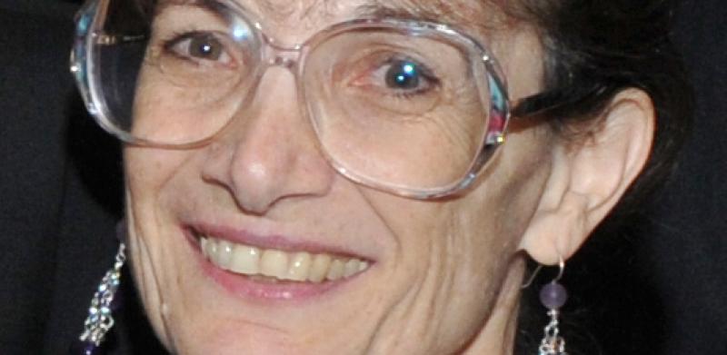 Photograph of a smiling woman wearing large glasses and dangling earrings.