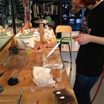 A jeweler works with a soldering torch at a wooden workbench.