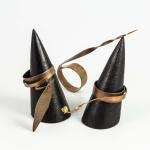Unusual copper rings displayed on black conical stands against a white background.