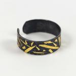 Black metal bracelet with an open back and jagged gold inlay on a white background.